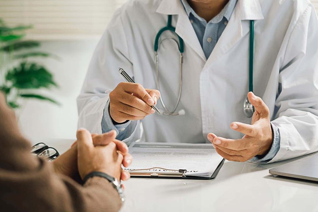 A professional physician in a white medical uniform talks to discuss results or symptoms and gives a recommendation to a male patient and signs a medical paper at an appointment visit in the clinic.